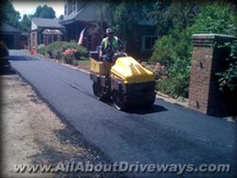 an innovative new asphalt driveway being set up plus the roller compacting the asphalt while it's hot